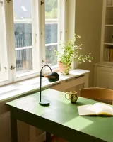 DC Portable Bordlampe Mørkegrøn fra Halo Design på et skrivebord ved et vindue DC Portable Bordlampe Mørkegrøn fra Halo Design på et skrivebord ved et vindue